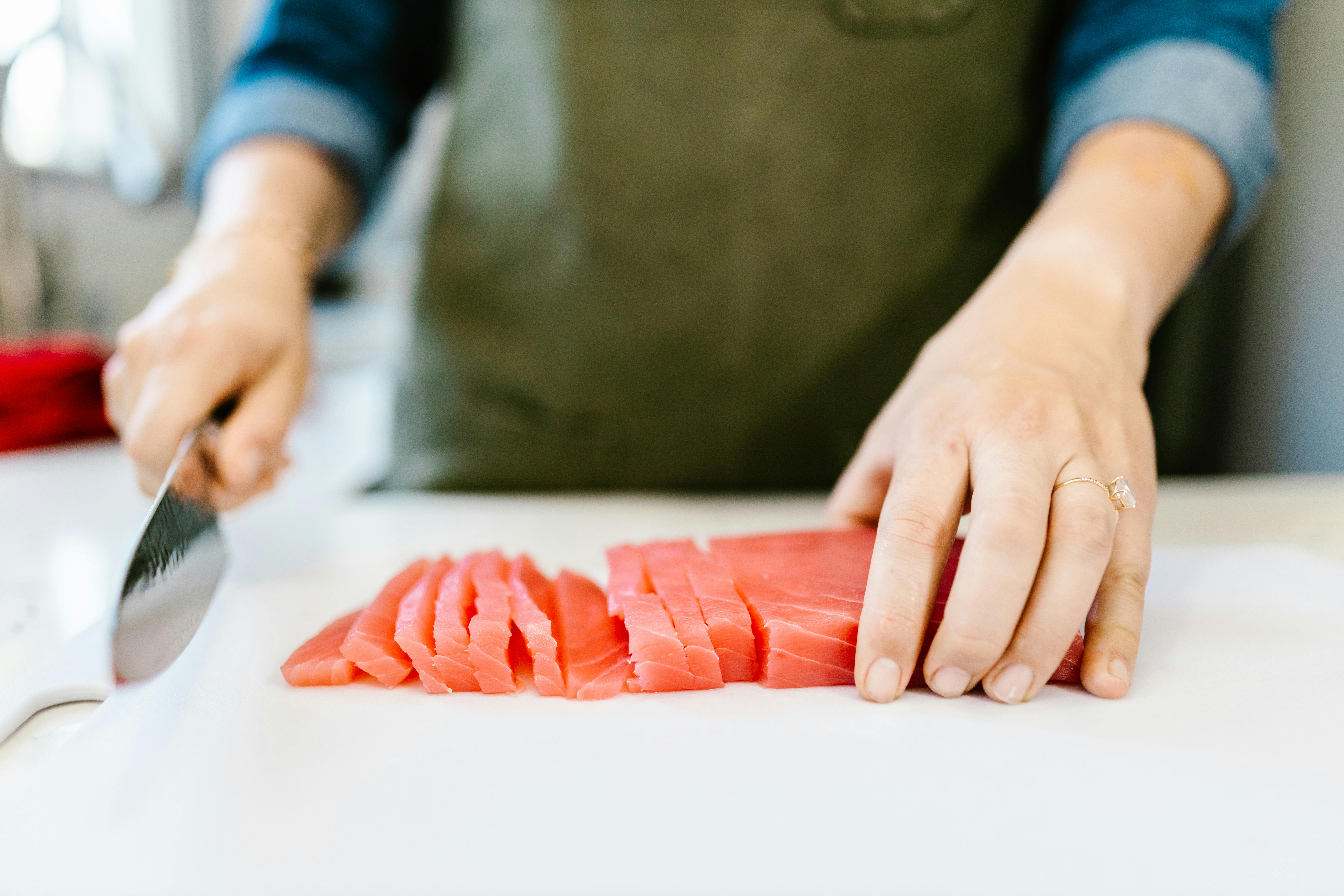 Close-up of hands slicing fresh salmon fillet on a cutting board, ideal for seafood and cooking content.